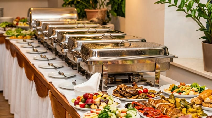 A long buffet table with chafing dishes, plates, and various dishes of food.