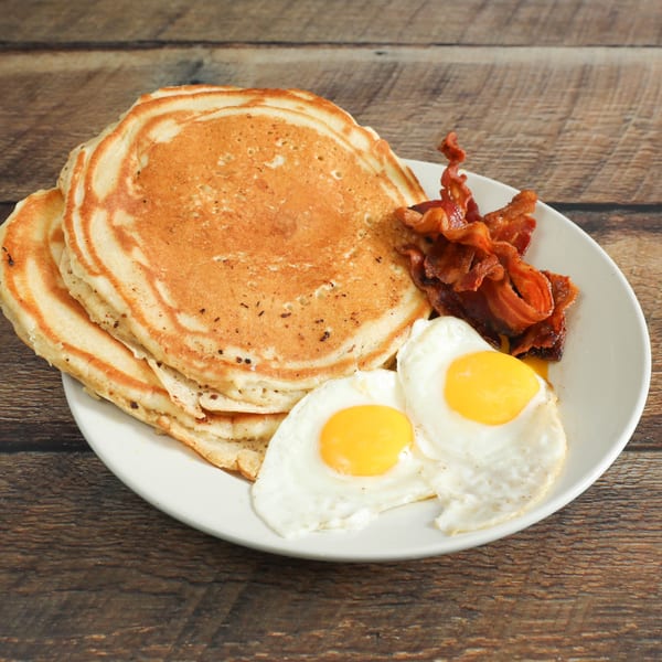 A breakfast plate with a stack of pancakes, crispy bacon, and two sunny-side-up eggs.