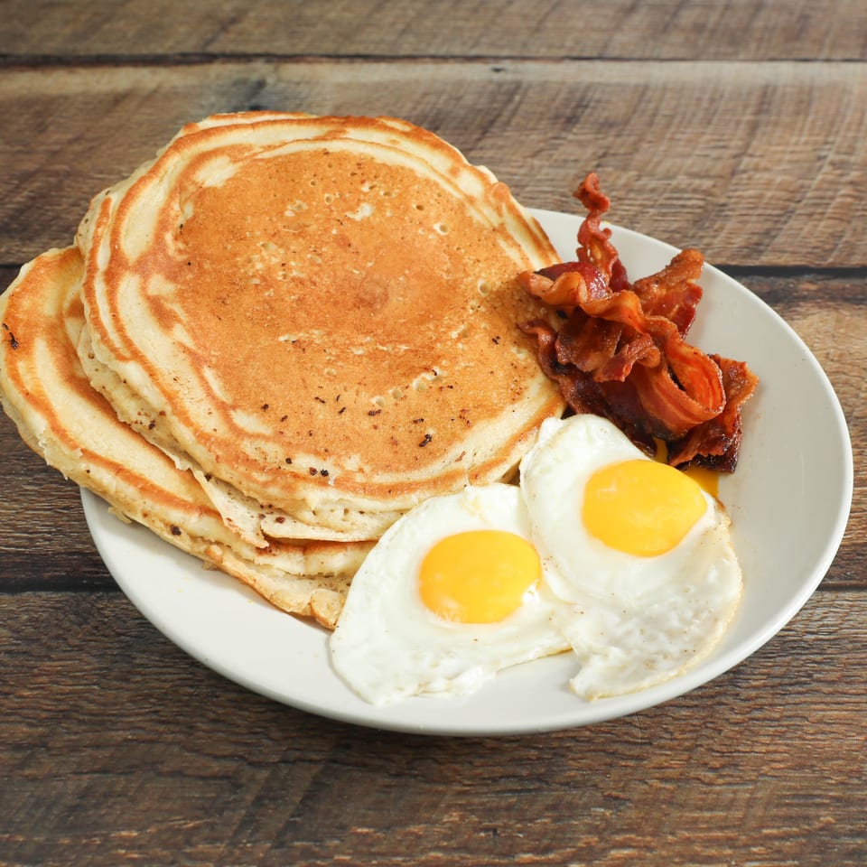 A breakfast plate with a stack of pancakes, crispy bacon, and two sunny-side-up eggs.