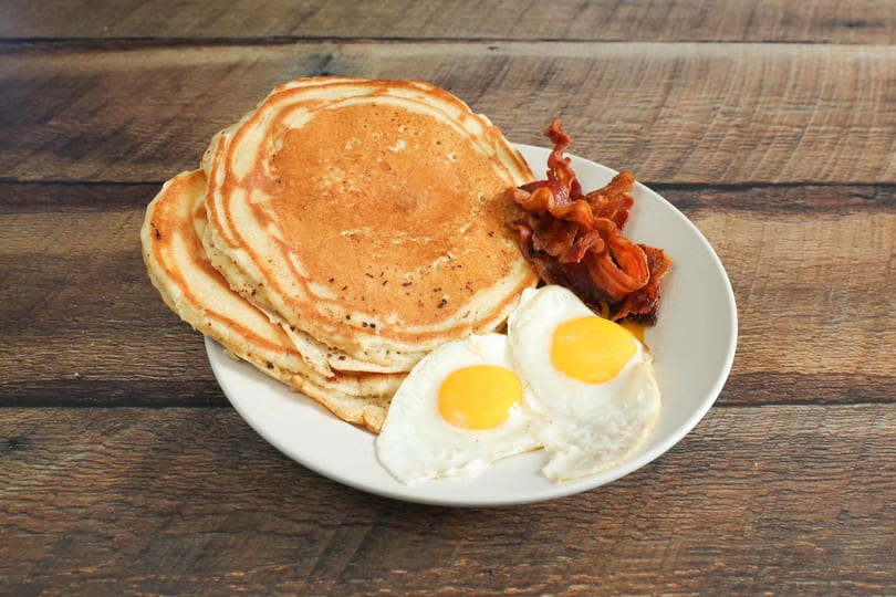 A breakfast plate with a stack of pancakes, crispy bacon, and two sunny-side-up eggs.